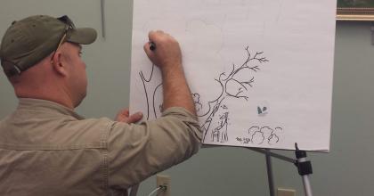 a man drawing a picture of a forest on a flip chart